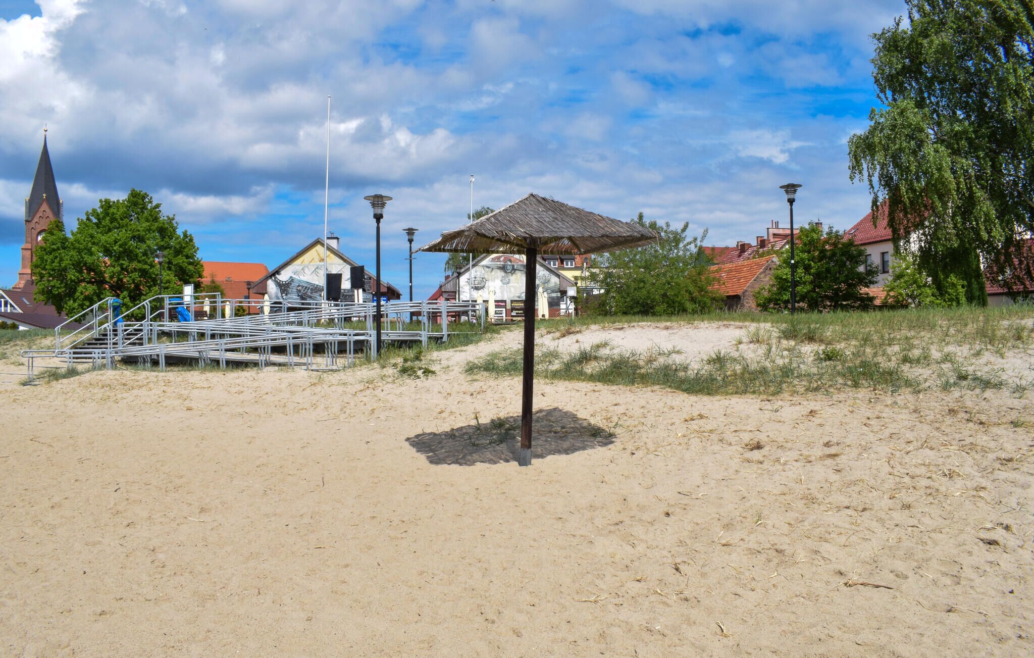 En strand med ett parasoll av halmtak, en kyrka och en byggnad med en väggmålning.