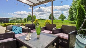 An outdoor patio with wicker furniture, a glass-top table, and string lights. - Awesome home in Nowe Warpno with house sea view (Nowe Warpno)