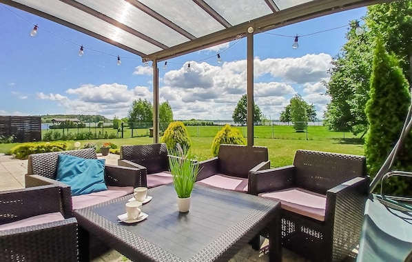An outdoor patio with wicker furniture, a glass-top table, and string lights.