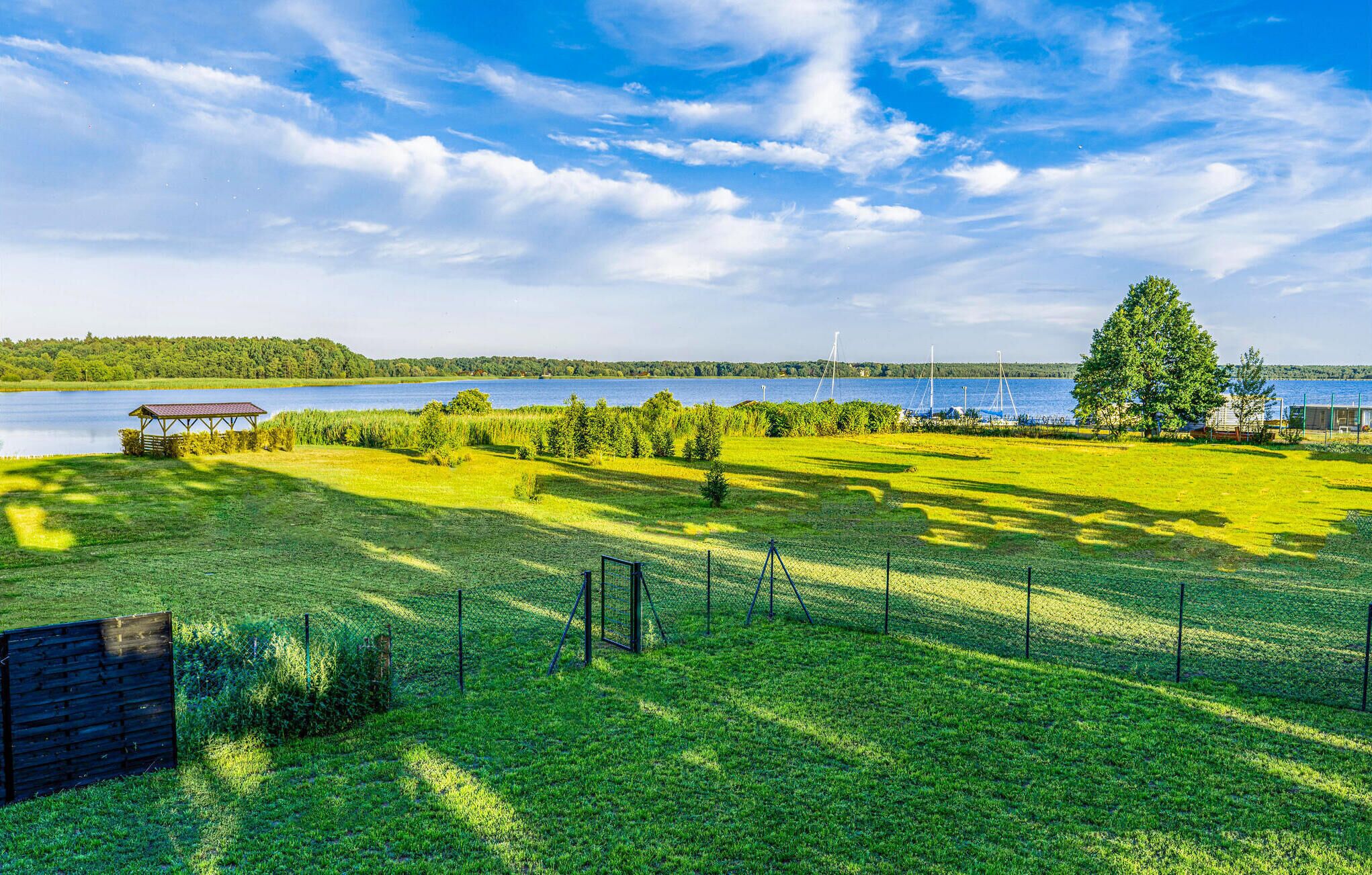 Een grasveld met een houten constructie, een omheind gebied en een waterpartij op de achtergrond.