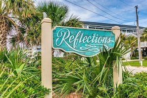 A sign with the word "Reflections" in cursive script, surrounded by lush greenery.