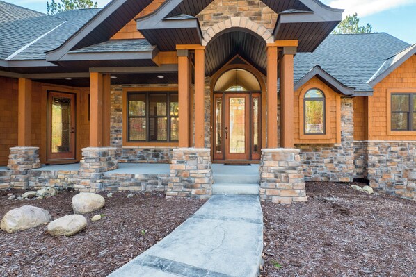A modern house with a stone facade, a central entrance with a glass door, and a stone pathway leading to the front door.