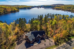 A cabin with a sloped roof, surrounded by a forest with autumn foliage, and a large body of water in the background. - Lakefront Retreat at Giants Ridge: Golf, Hike, Ski (Biwabik)