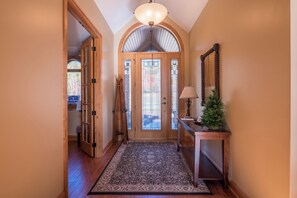 A hallway with a wooden door, a rug, a lamp, and a small Christmas tree.