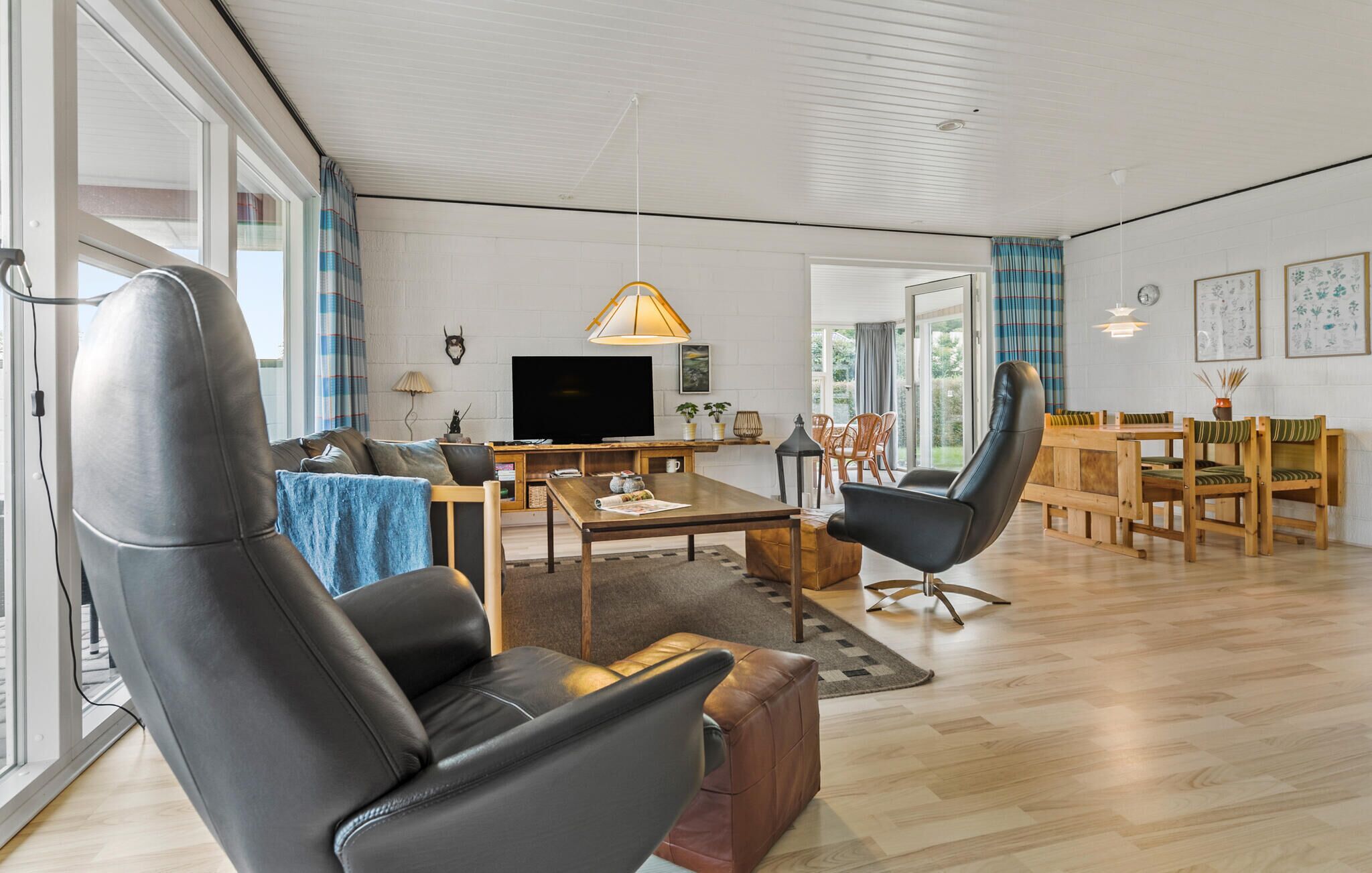 Ein modernes Wohnzimmer mit einer Couch, einem Couchtisch und einem Fernseher. Es gibt einen Essbereich mit Tisch und Stühlen.