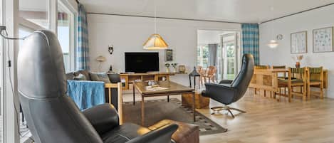 A modern living room with a sofa, a coffee table, and a TV. There is a dining area with a table and chairs.