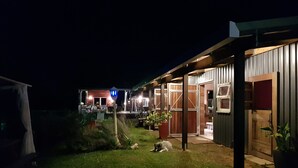 A well-lit outdoor area with a covered seating area, a dog lying on the grass, and a building with large windows and doors. - The Shed Conversion with Hot tub and amazing views: Building#5 (Austinville)