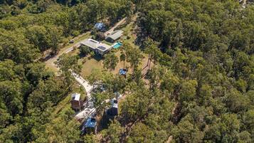 Vue aérienne d’une propriété comprenant plusieurs bâtiments, entourée d’une forêt dense. On y distingue différentes constructions, notamment un grand bâtiment doté d’un toit vert et des bâtiments plus petits avec des toits bleus.