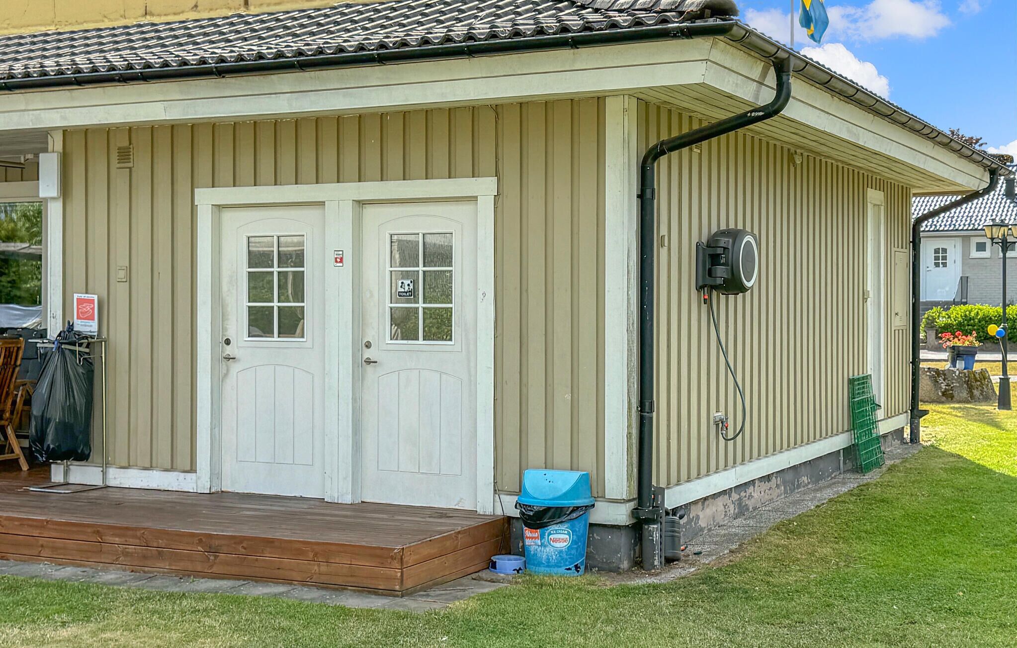 A building with two white doors, a small porch, a trash bin, and a security camera.