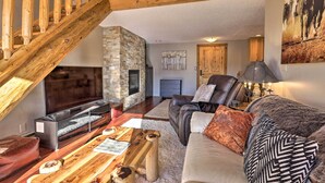 A cozy living room with a stone fireplace, wooden staircase, leather sofa, and a flat-screen TV. - Steamboat Ski Getaway w/ Balcony & Resort Views! (Steamboat Springs)