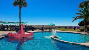 A swimming pool with a pink flamingo float, palm trees, and a covered seating area. - Lloyd's Lodge: Spacious Fripp Island Retreat with Golf, Beaches, Pools, and Screened Porch! (Fripp Island)