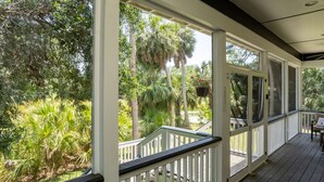 A covered porch with white railings and a wooden deck, overlooking a lush garden with various tropical plants and trees. - Lloyd's Lodge: Spacious Fripp Island Retreat with Golf, Beaches, Pools, and Screened Porch! (Fripp Island)