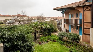 Zona residencial con una casa que tiene balcón, un jardín con diversas plantas y una calle con coches aparcados.