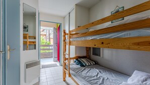 Un dormitorio con literas, una puerta que da a un área exterior, un espejo y una ventana pequeña con vistas a la vegetación.