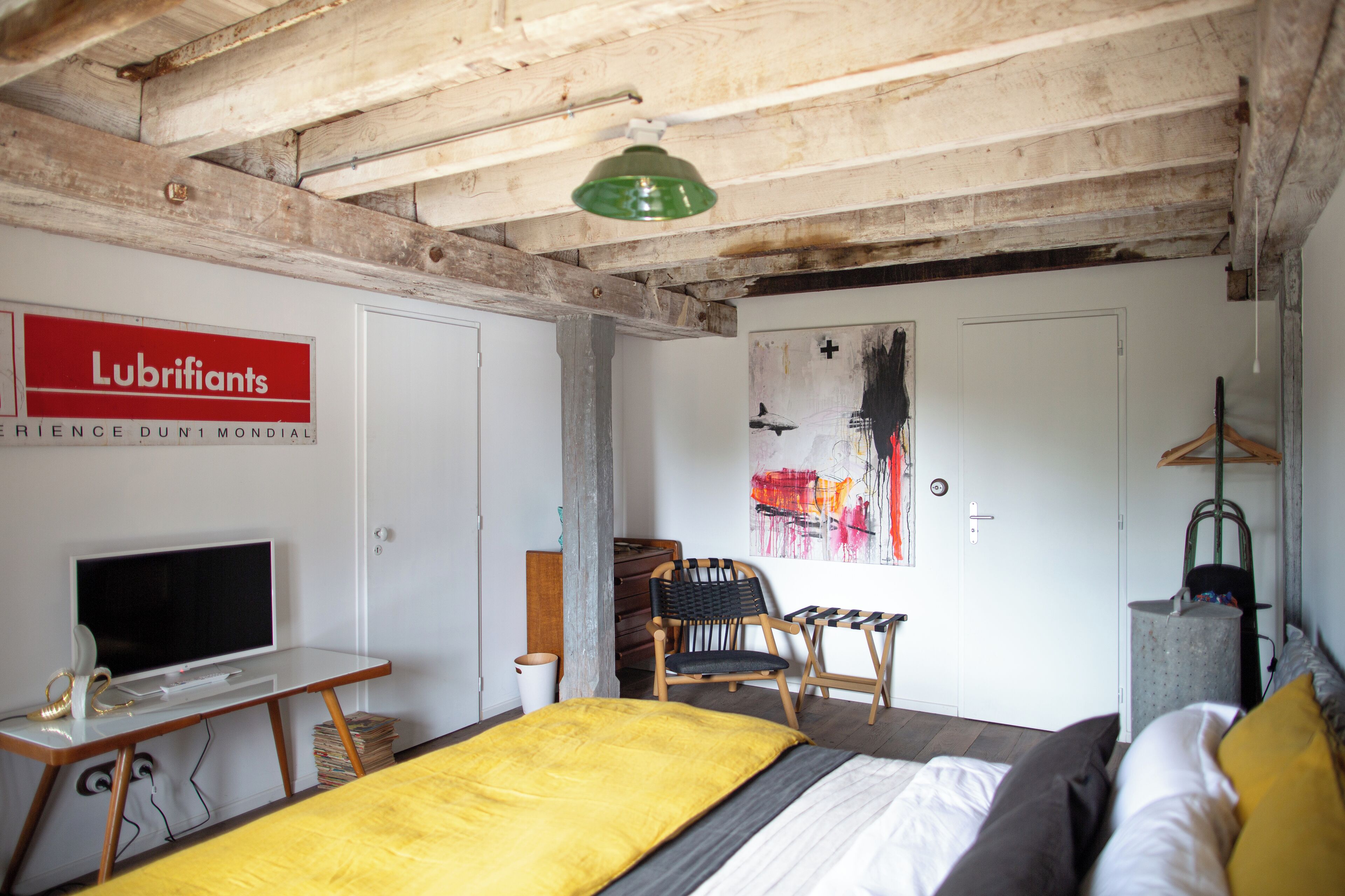 Une chambre à coucher avec un lit, un bureau avec un ordinateur, une chaise, un porte-manteau et une porte ornée d’un tableau.