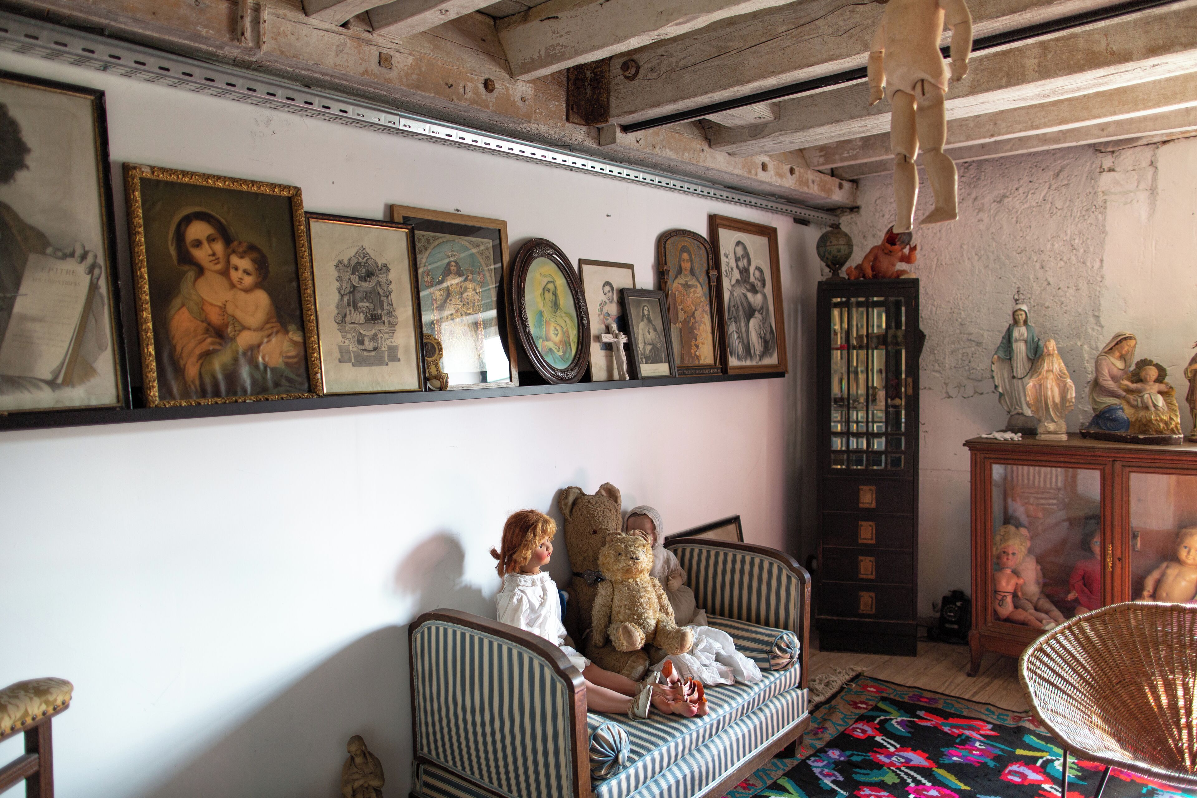A room with a sofa, a chair, and a wall adorned with framed pictures and statues.