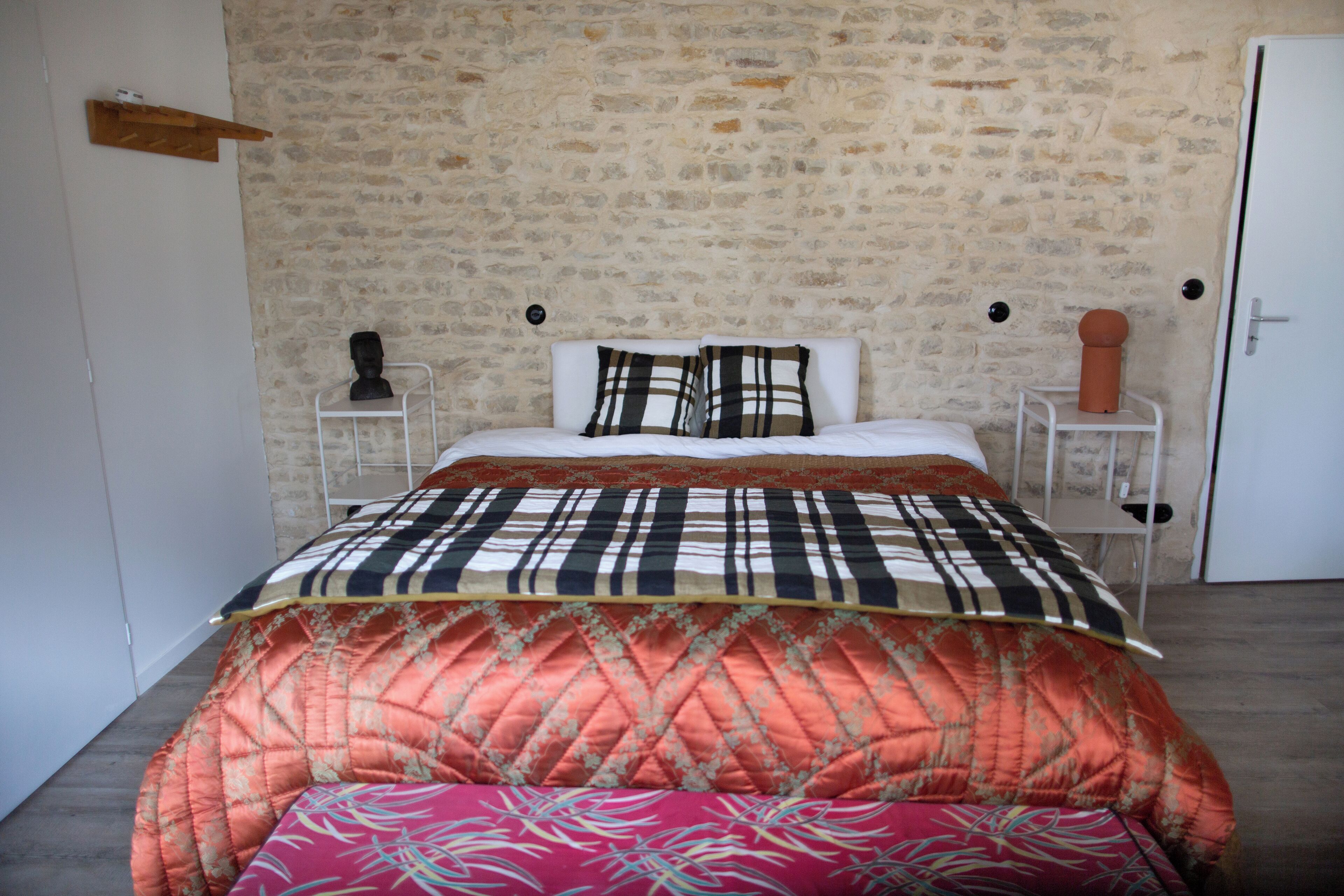 A bed with a plaid bedspread, a white headboard, and a bench at the foot of the bed.