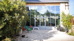 A modern building with large glass windows, a gravel patio, and outdoor seating. - Former flour mill 20 minutes from La Rochelle: sleeps 15 to 25 (mauzé on the mignon)