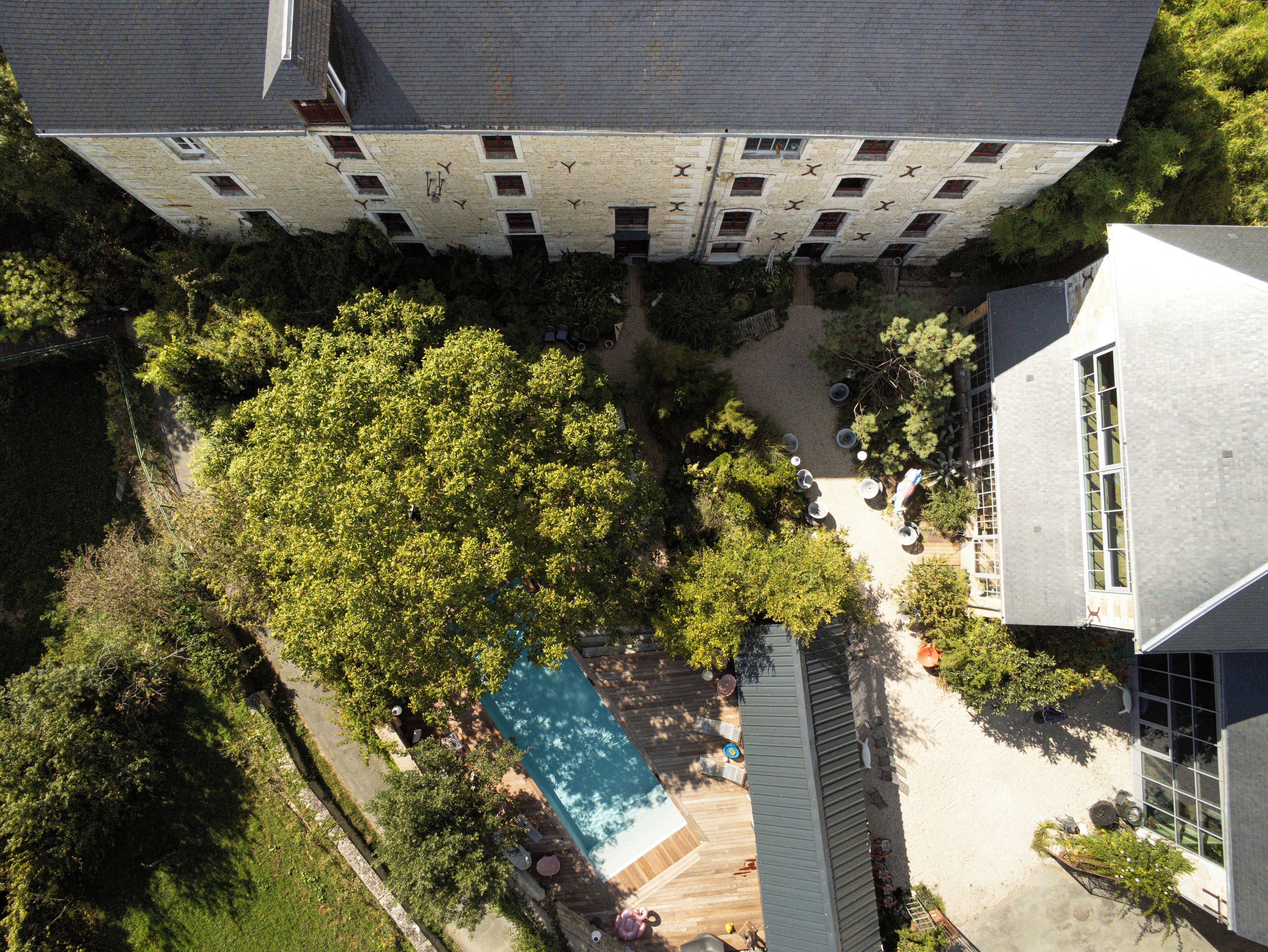 An aerial view of a property with a swimming pool, surrounded by trees and a large building with multiple windows.