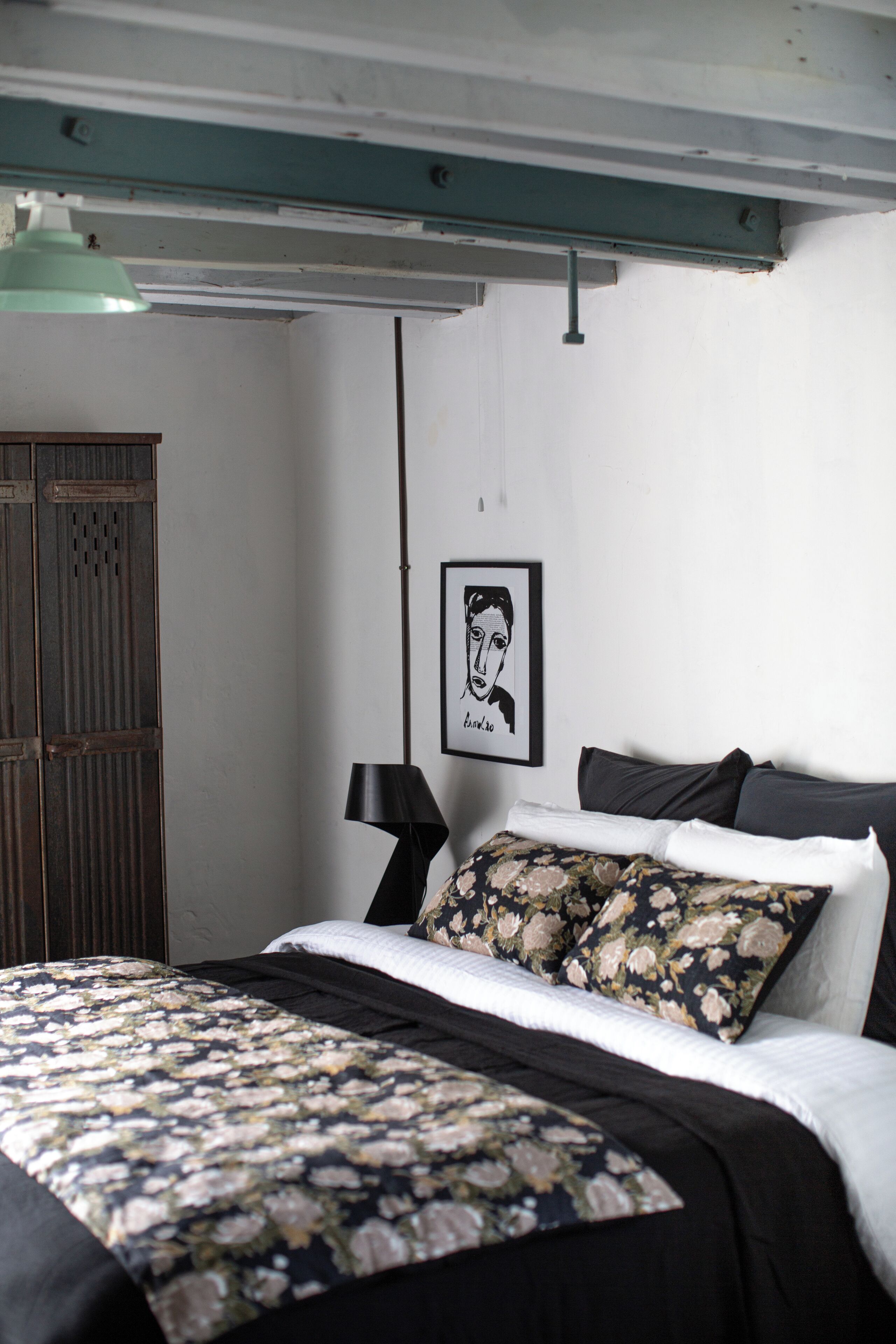 Een slaapkamer met een bed, nachtkastje, lamp, een ingelijst schilderij aan de muur en een kledingkast.
