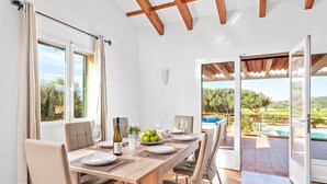 Un comedor con una mesa de madera dispuesta para cuatro, una botella de vino y un bol de fruta.