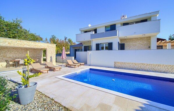Una casa moderna de dos pisos con piscina, mobiliario exterior y un muro de piedra.