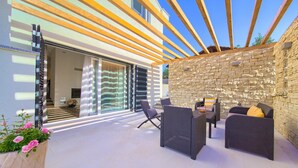 An outdoor patio with wicker furniture, a stone wall, and a wooden pergola. - Luxurious home in Risika (Risika)
