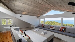 A modern bedroom with a skylight, a large bed, a bench with cushions, a sink, and a view of the sea. - 5 bedroom beach front home in Blato (Blato)