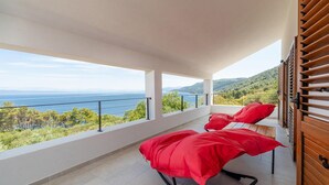 A balcony with two red bean bags, a view of the sea and hills, and a wooden door. - 5 bedroom beach front home in Blato (Blato)