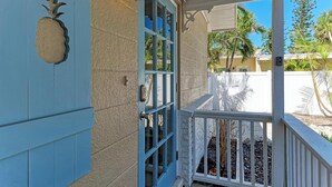 Una casa con puerta azul, una decoración de piña y barandilla blanca.