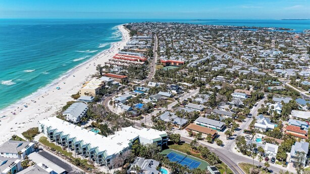 Vista aérea de una zona residencial costera con propiedades frente a la playa, una avenida principal y una cancha de tenis.