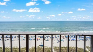 A beach with umbrellas and people, viewed from a balcony.