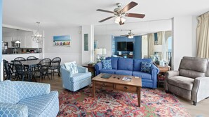 A living room with a blue sofa, patterned armchairs, a coffee table, and a red patterned rug.