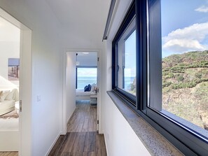 Ein schmales Gang mit einem Bett und Blick auf das Meer durch ein großes Fenster.
