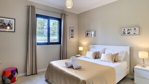 A hotel room with a bed, bedside tables, a window with curtains, and wall art. - Apartment Lotus by LovelyStay (Funchal)