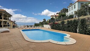 A swimming pool with lounge chairs, a tiled deck, and buildings in the background. - Apartment Lotus by LovelyStay (Funchal)