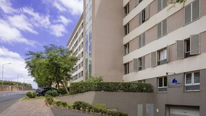Un edificio moderno de varios pisos con fachada plana, grandes ventanales y un estacionamiento con algunos coches.