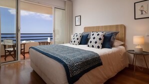 Habitación de hotel con cama, una silla, una mesa y vista al océano a través de una puerta corrediza.