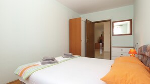 A bedroom with a bed, a nightstand, a lamp, a mirror, and a door leading to another room.