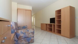 A spacious room with a sofa, wooden cabinets, and a TV on a stand.