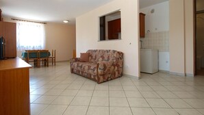 A living room with a sofa, a dining table with chairs, a kitchen area with cabinets, and a small refrigerator. - Apartment 1842/23312 (Istria - Fažana), 50m from the beach (Fažana)