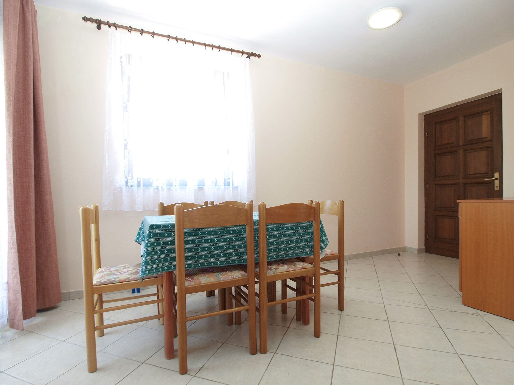 Un coin repas comprenant une table et quatre chaises, une porte en bois et une fenêtre avec des rideaux.