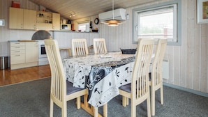 A compact kitchen with wooden cabinets, a dining table with chairs, and a window providing natural light. - 3 bedroom cozy home in Hemmet (Hemmet)