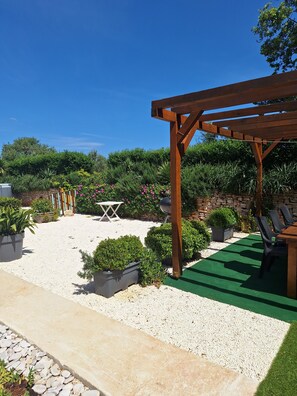 A garden patio with a pergola, seating area, and various potted plants.
