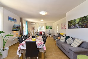 Een eetgedeelte met een tafel voor zes personen, een grijze bank en een aan de muur bevestigde televisie.