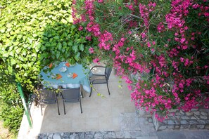 An outdoor dining area with a table set for two, surrounded by lush greenery and vibrant pink flowers. - Apartment 2023/28732 (Istria - Rabac), 500m from the beach (Rabac)