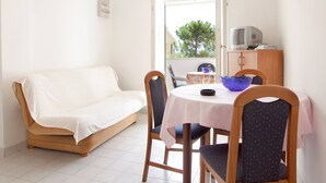 A small, cozy room with a sofa, a dining table with chairs, a TV, and a cabinet.