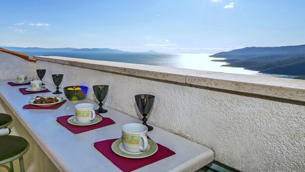 A table set with plates, cups, and glasses on a balcony overlooking a body of water and distant hills. - Apartment 2024/28742 (Istria - Rabac), 1200m from the beach (Rabac)