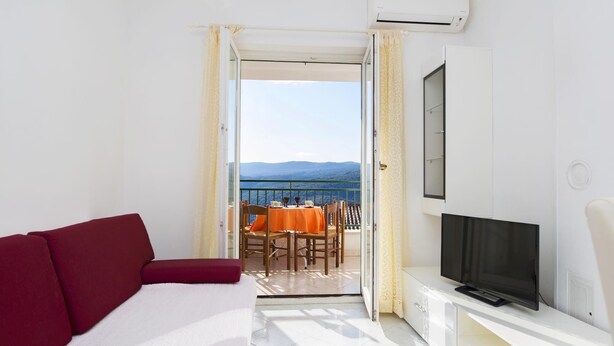 A hotel room with a red sofa, a TV on a white cabinet, and a balcony with a table and chairs. - Apartment 2024/28745 (Istria - Rabac), 1200m from the beach (Rabac)