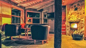 Ett mysigt rum med en öppen spis i sten, ett träpanelat tak och en matplats med ett bord och stolar.